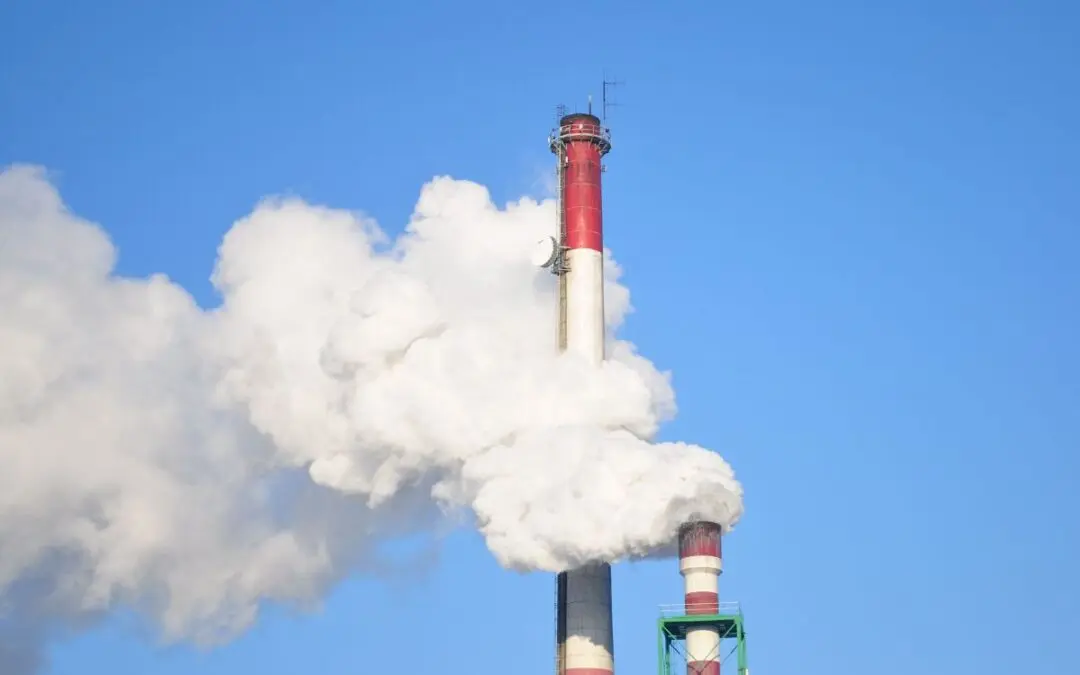 Industriële schoorstenen met een zichtbare witte emissiepluim tegen een blauwe lucht.