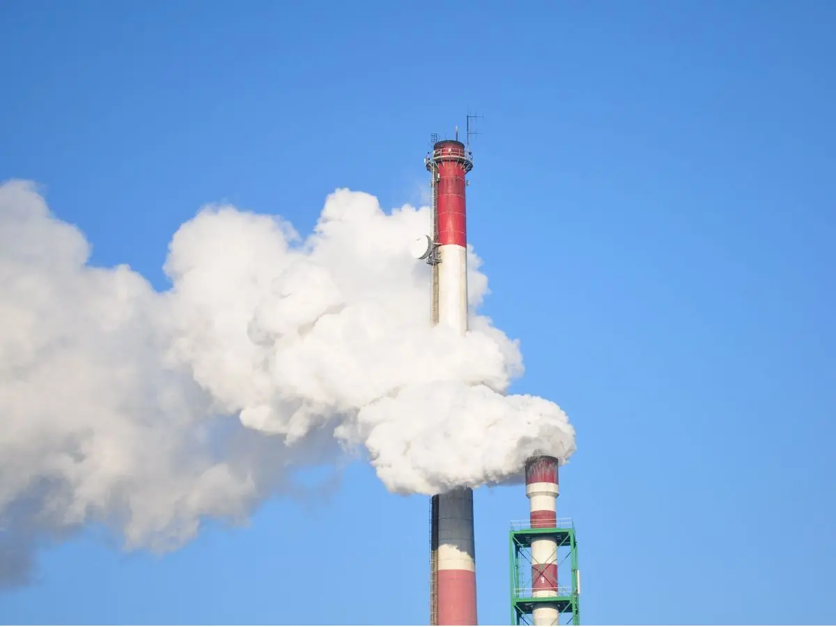 Industriële schoorstenen met een zichtbare witte emissiepluim tegen een blauwe lucht.